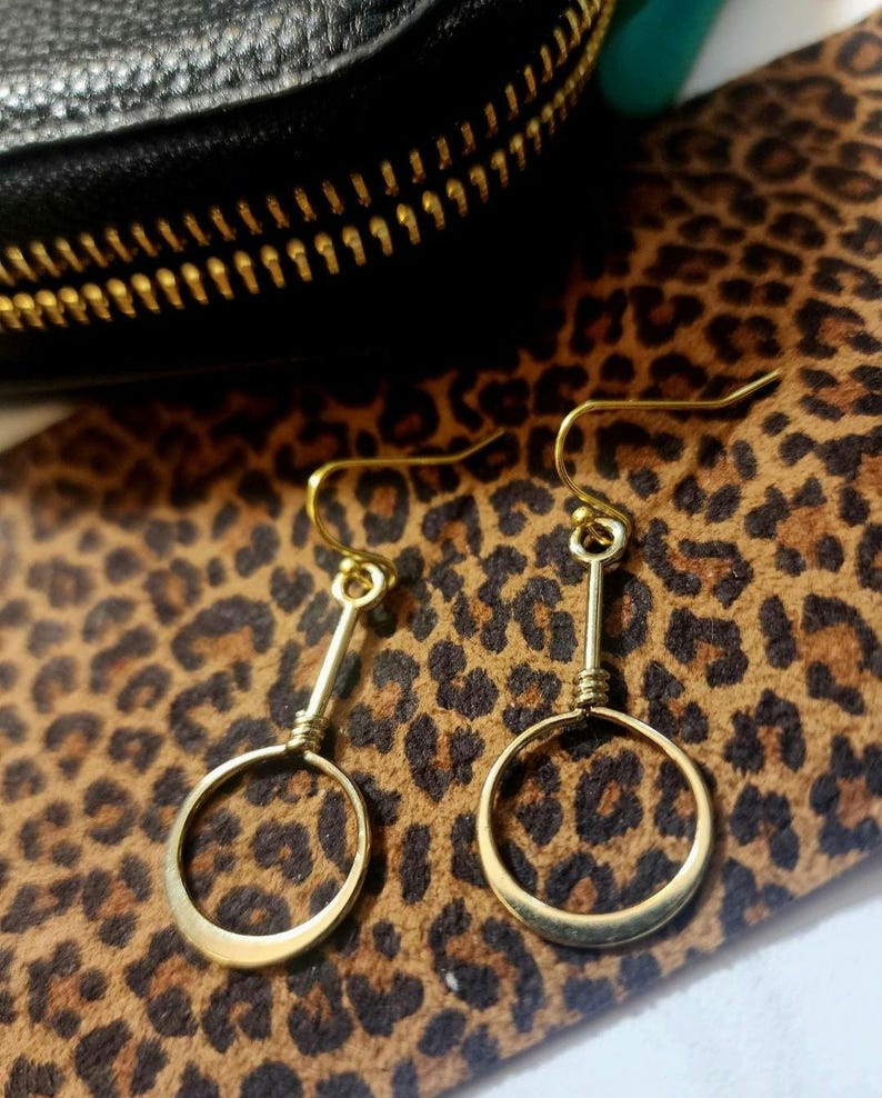 May include: A pair of gold hoop earrings with a simple, minimalist design. The hoops are suspended from a straight wire, creating a delicate and modern look.