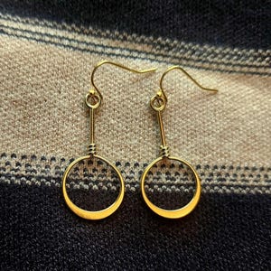 May include: A pair of gold hoop earrings with a simple, minimalist design. The hoops are circular and have a smooth, polished finish.
