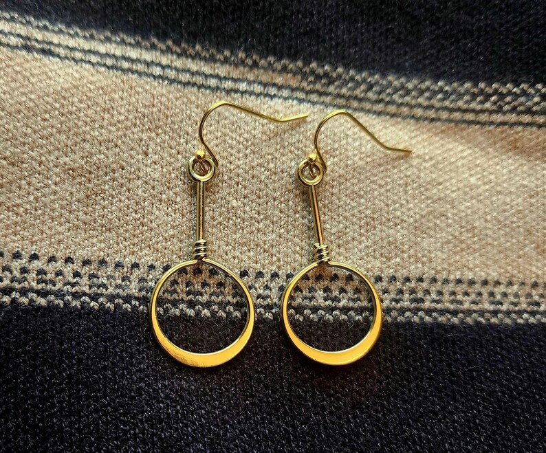 May include: A pair of gold hoop earrings with a simple, minimalist design. The hoops are circular and have a smooth, polished finish.