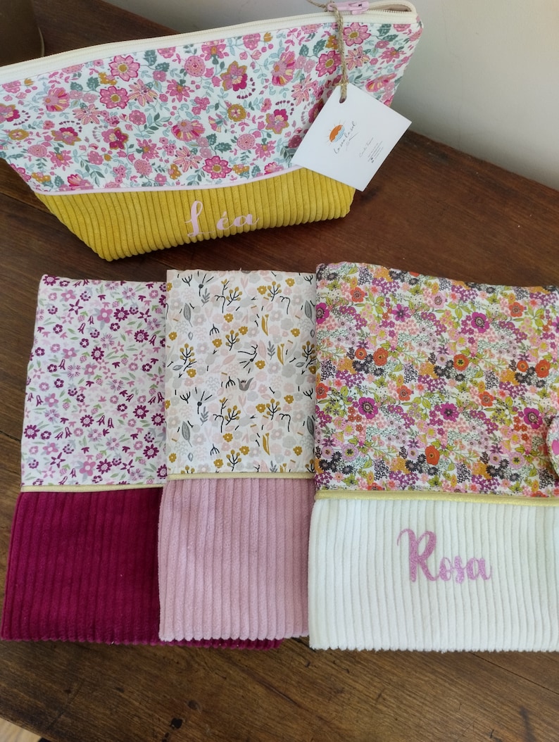 May include: Three floral fabric pouches with yellow, pink, and white corduroy bottoms. The pouches are personalized with the names "L&eacute;a", "Rosa", and a third name that is not visible in the image.