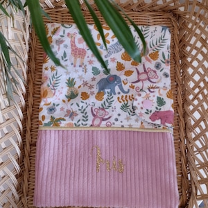 May include: Pink and white baby blanket with a jungle animal print and the name "Iris" embroidered in gold thread.