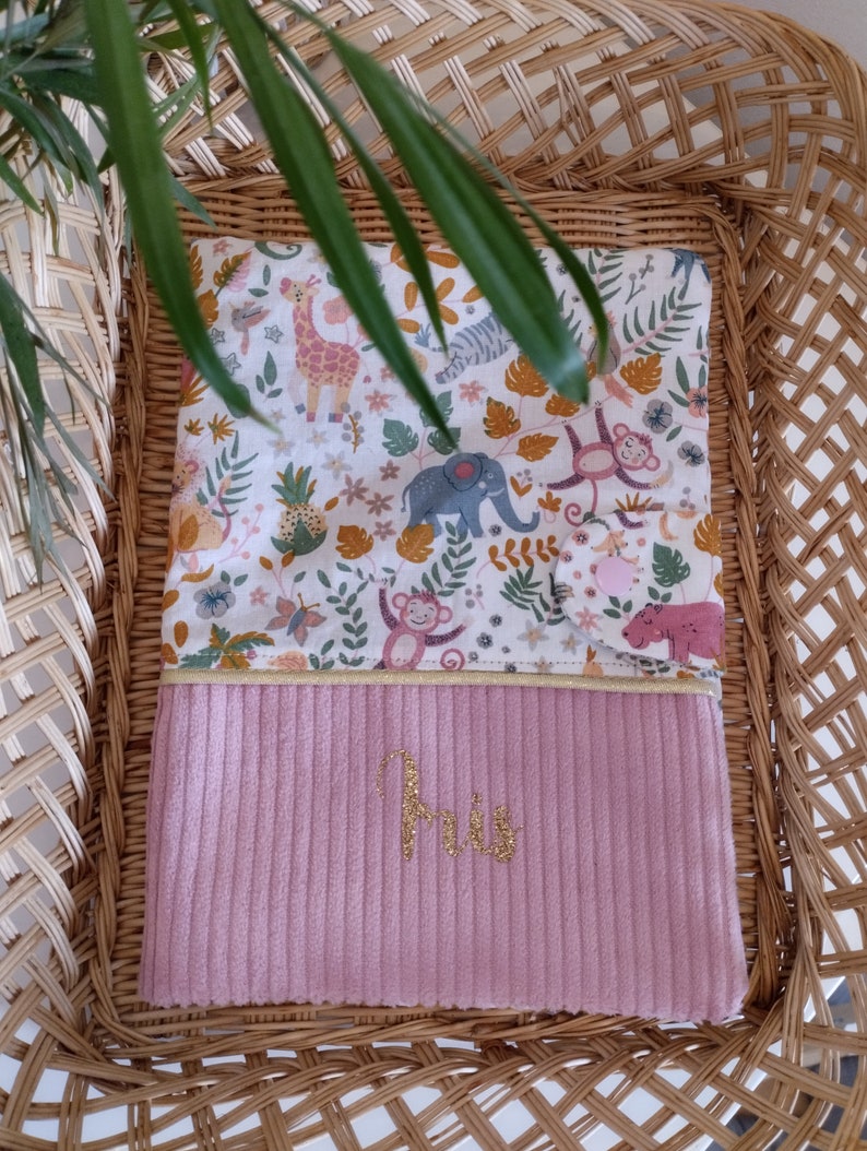 May include: Pink and white baby blanket with a jungle animal print and the name "Iris" embroidered in gold thread.