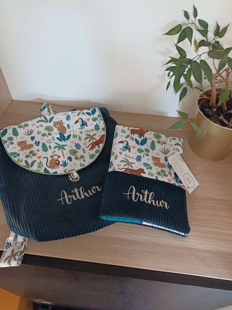 May include: A dark blue backpack and a matching book bag with a jungle animal print and the name "Arthur" embroidered on each.