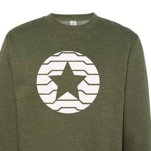 Puede incluir: Sudadera verde oliva con cuello redondo y dise&ntilde;o de estrella blanca dentro de un patr&oacute;n circular. La estrella est&aacute; centrada dentro del c&iacute;rculo. La sudadera tiene mangas largas y cuello, pu&ntilde;os y dobladillo acanalados. El dise&ntilde;o est&aacute; impreso en la parte delantera.