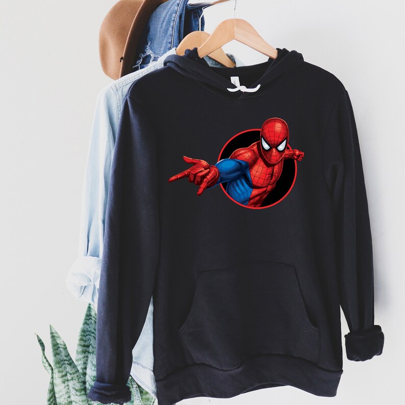 May include: Black hooded sweatshirt featuring a graphic of Spider-Man in a red and blue suit, set against a black circle. The superhero is depicted with his arm extended, pointing. The sweatshirt has a front pocket and a drawstring hood.