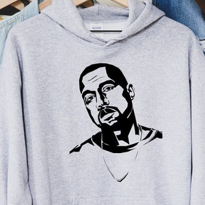 Op de afbeelding: Een lichtgrijze hoodie met een zwart-wit grafisch portret. Het portret is van een man met een baard en een ketting. De hoodie hangt aan een houten hanger.