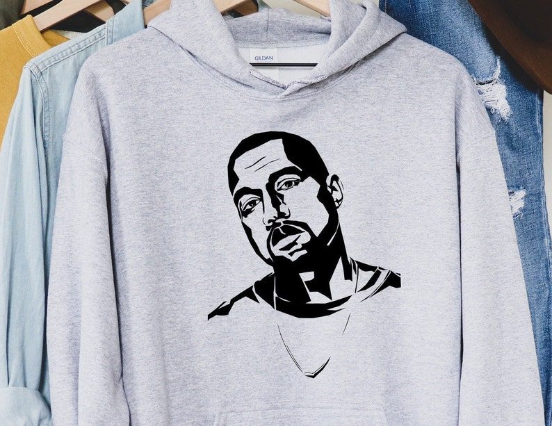 Op de afbeelding: Een lichtgrijze hoodie met een zwart-wit grafisch portret. Het portret is van een man met een baard en een ketting. De hoodie hangt aan een houten hanger.