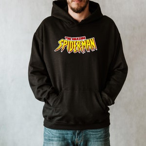 May include: Black hooded sweatshirt with the text "THE AMAZING SPIDER-MAN" in red and yellow lettering. The sweatshirt has a front pocket and a drawstring hood. The design is centered on the chest.
