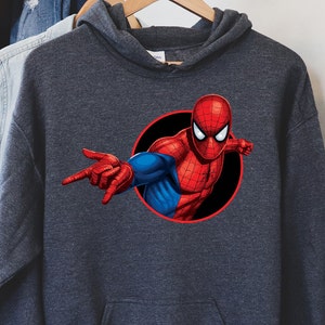 May include: Dark gray hooded sweatshirt featuring a vibrant graphic of Spider-Man. The superhero is depicted in his classic red and blue suit, emerging from a black circle. The design showcases Spider-Man's iconic pose, with one hand outstretched.