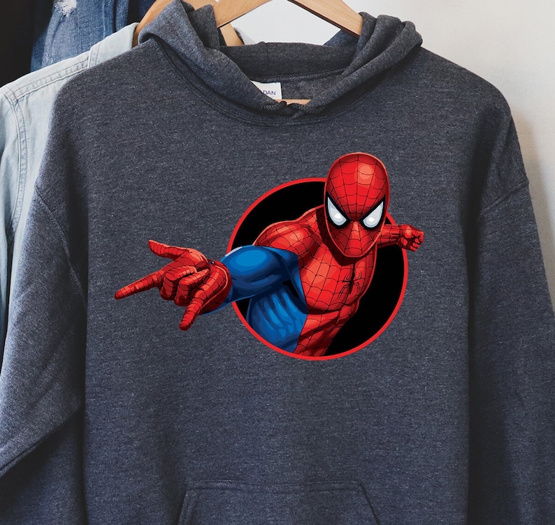 May include: Dark gray hooded sweatshirt featuring a vibrant graphic of Spider-Man. The superhero is depicted in his classic red and blue suit, emerging from a black circle. The design showcases Spider-Man's iconic pose, with one hand outstretched.