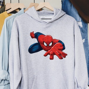 K&ouml;nnte beinhalten: Hellgrauer Kapuzenpullover mit einem gro&szlig;en Aufdruck von Spider-Man. Der Superheld ist in seinem klassischen rot-blauen Anzug dargestellt, mit ausgestreckten H&auml;nden. Der Kapuzenpullover hat eine Vordertasche und eine Kapuze.