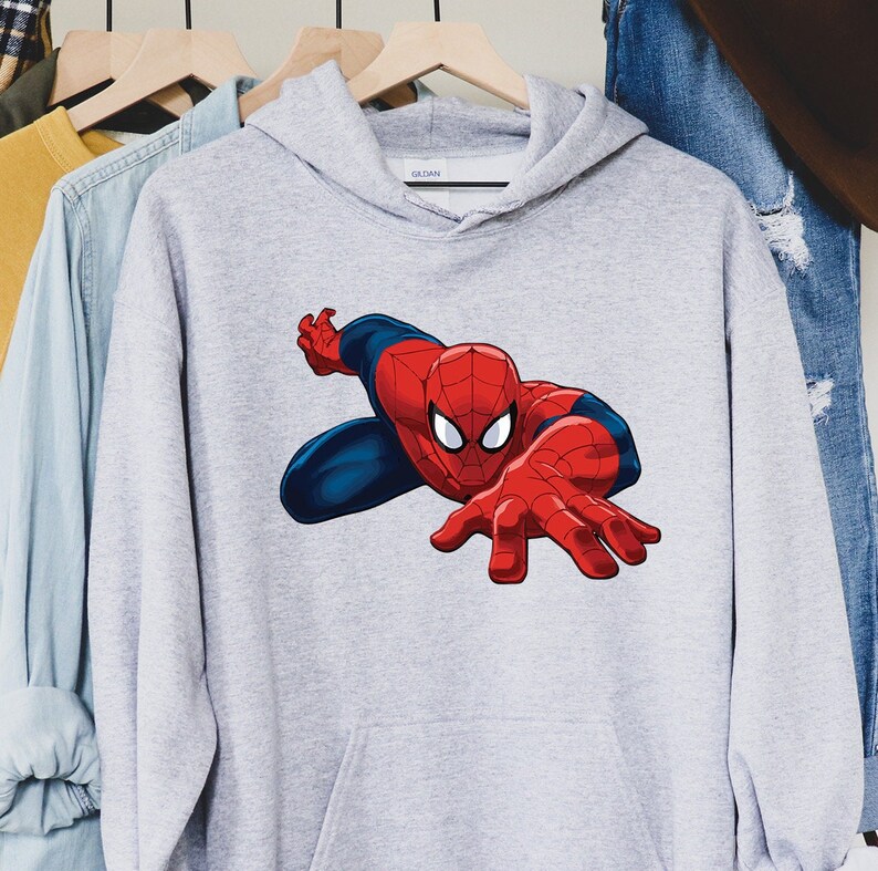 K&ouml;nnte beinhalten: Hellgrauer Kapuzenpullover mit einem gro&szlig;en Aufdruck von Spider-Man. Der Superheld ist in seinem klassischen rot-blauen Anzug dargestellt, mit ausgestreckten H&auml;nden. Der Kapuzenpullover hat eine Vordertasche und eine Kapuze.