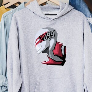 May include: A light gray hoodie featuring a futuristic illustration of a helmet with the number "2099" in red and white. The design is a stylized graphic with red and gray accents. The hoodie is hanging on a wooden hanger.