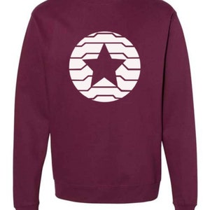 Puede incluir: Sudadera burdeos con un dise&ntilde;o de estrella blanca dentro de un c&iacute;rculo. La estrella est&aacute; centrada y el c&iacute;rculo est&aacute; formado por l&iacute;neas horizontales. La sudadera tiene cuello redondo y mangas largas.