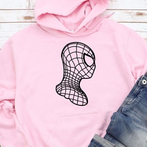 Op de afbeelding: Een lichtroze hoodie met een zwarte afbeelding van een gestileerd Spider-Man-masker. Het ontwerp is een zijaanzicht met een webachtig patroon. De hoodie heeft een voorzak en een capuchon. Jeans zijn zichtbaar.