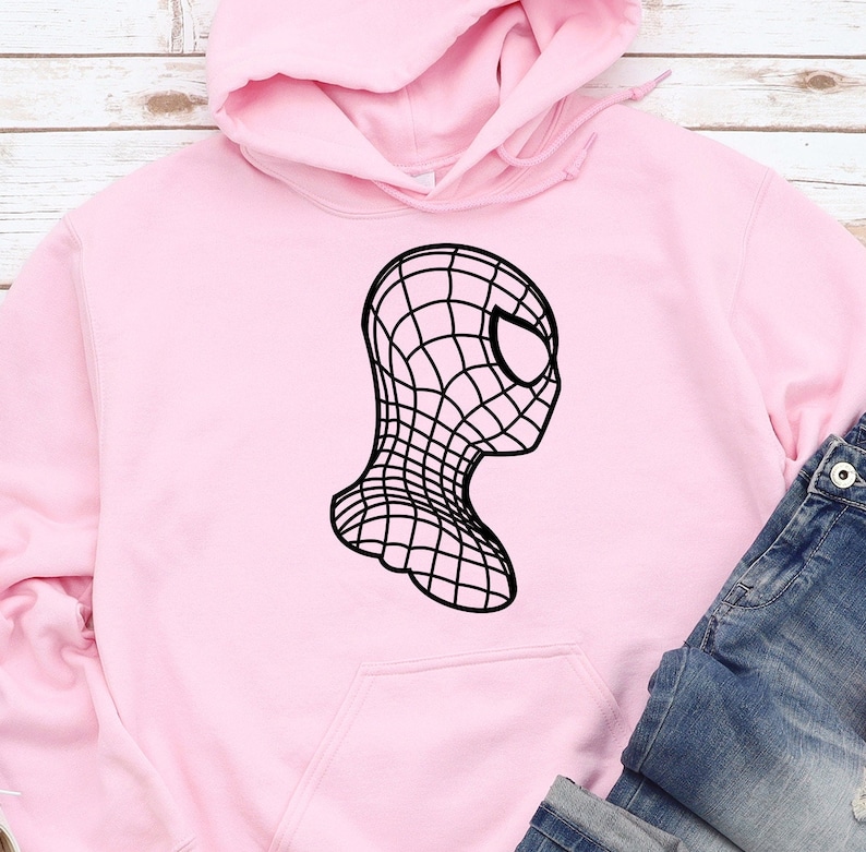 Op de afbeelding: Een lichtroze hoodie met een zwarte afbeelding van een gestileerd Spider-Man-masker. Het ontwerp is een zijaanzicht met een webachtig patroon. De hoodie heeft een voorzak en een capuchon. Jeans zijn zichtbaar.
