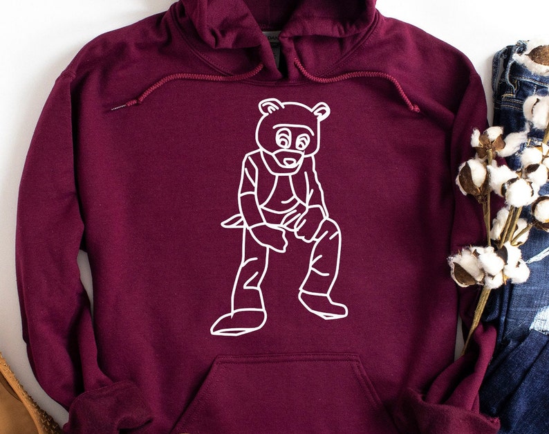 Pu&ograve; includere: Una felpa con cappuccio bordeaux con un'illustrazione a contorno bianco di un orso. L'orso indossa un costume ed &egrave; seduto. La felpa ha un cordino e una tasca frontale.