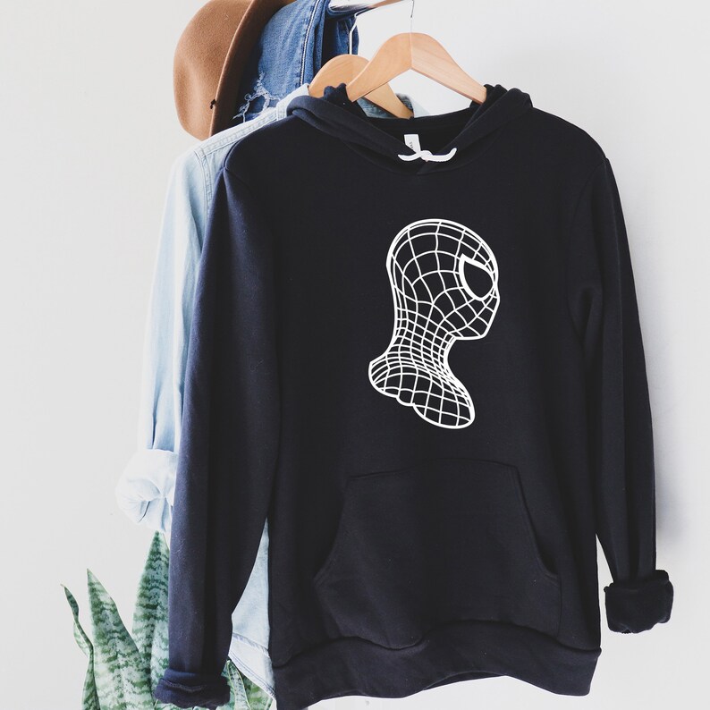 Op de afbeelding: Zwarte hoodie met een witte afbeelding van een gestileerde Spider-Man-kop. Het ontwerp heeft een rasterpatroon, waardoor een 3D-effect ontstaat. De hoodie heeft een voorzak en een wit trekkoord.