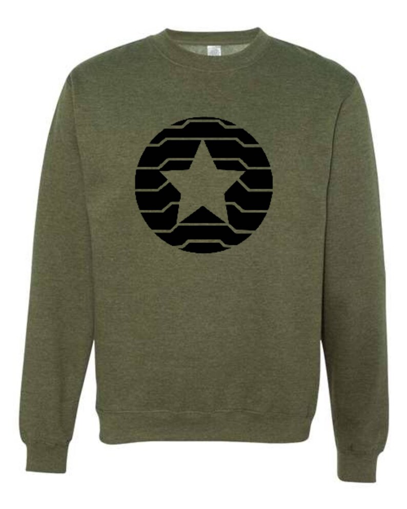 Puede incluir: Sudadera verde oliva con un dise&ntilde;o de estrella negra dentro de un patr&oacute;n circular. La estrella est&aacute; centrada y el c&iacute;rculo est&aacute; compuesto por l&iacute;neas horizontales. La sudadera tiene cuello redondo y mangas largas, adecuada para uso casual.