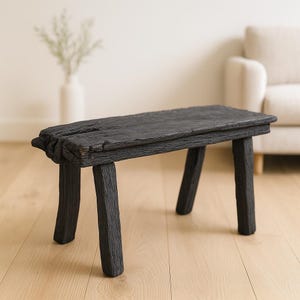 May include: A black wooden bench with a rectangular seat and four legs. The bench has a distressed, weathered look, with visible wood grain and an uneven surface. The legs are curved, adding to the bench's unique, handcrafted aesthetic. The bench is approximately 100 cm long.