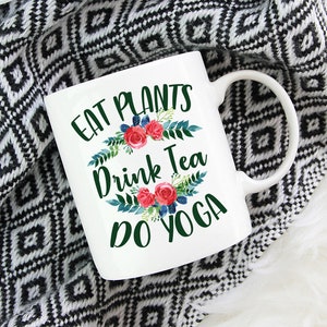 May include: White ceramic mug with a green, floral design and the text "Eat Plants Drink Tea Do Yoga".