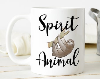 May include: A white ceramic mug featuring a brown watercolor illustration of a sloth hanging from a branch. The text "Spirit Animal" is printed in black cursive script above and below the sloth illustration on the front of the mug.