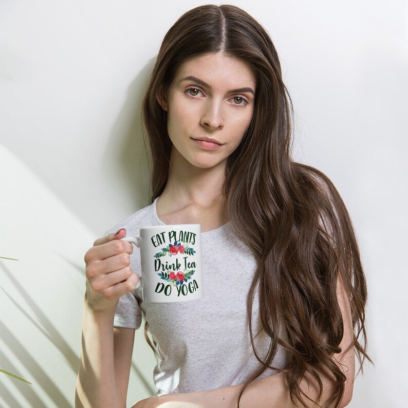May include: White ceramic mug with a floral design and the text "Eat Plants Drink Tea Do Yoga".