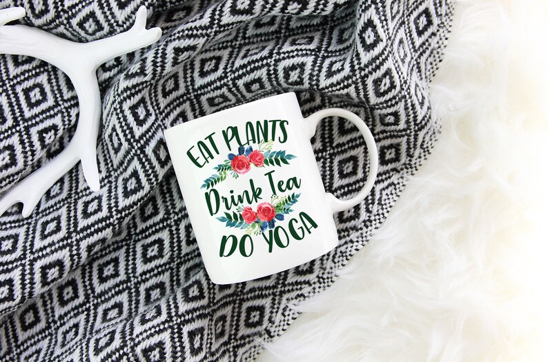 May include: White ceramic mug with a green, floral design and the text "Eat Plants Drink Tea Do Yoga".