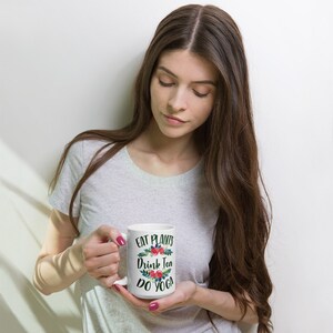 May include: White ceramic mug with a floral design and the text "Eat Plants Drink Tea Do Yoga".