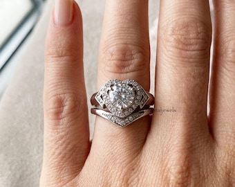 Könnte beinhalten: Ein silberfarbenes Ring-Set mit einem runden Mittelstein, der von einem herzförmigen Heiligenschein aus kleineren Steinen umgeben ist. Das Set enthält einen V-förmigen Konturring mit Pavé-Steinen. Der Text crystaljewels ist auf dem Ring sichtbar.