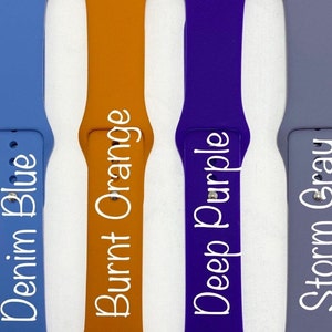 May include: Four silicone watch bands in different colors: denim blue, burnt orange, deep purple, and storm gray. Each band has the color name printed on it in white.