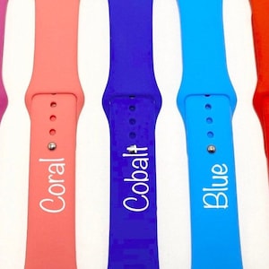 May include: Five different colored silicone watch bands with white text. The bands are fuchsia, coral, cobalt blue, blue, and red. The text on the bands reads "Fuschia", "Coral", "Cobalt", "Blue", and "Red".