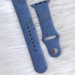 May include: A blue silicone Apple Watch band with a white floral and wolf design. The band has a moon and stars pattern.