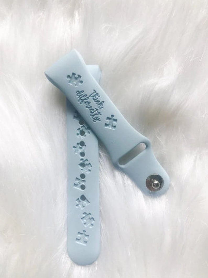 May include: A light blue silicone watch band with the text "Think Differently" and a puzzle piece design. The band has a silver metal buckle.