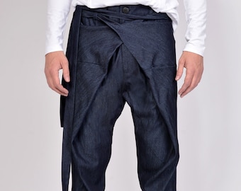 May include: Dark blue denim pants with a unique wrap-around design. The pants feature a high waist, a button closure, and a long, attached belt. The model is wearing black sneakers with white soles.