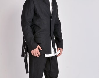 Puede incluir: Un blazer de lino negro con un diseño de cuello único, combinado con pantalones y sandalias negros a juego. El blazer presenta un cierre de un solo botón y detalles de correas. El atuendo es una versión moderna de un estilo clásico.