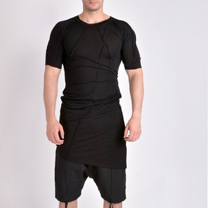 Può includere: Completo nero composto da top a maniche corte e pantaloncini. Il top presenta un design unico con cuciture a vista e orlo asimmetrico. I pantaloncini hanno dettagli con coulisse. L'outfit è abbinato a sneakers alte bianche e nere.