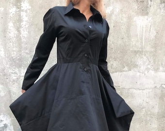 Könnte beinhalten: Ein schwarzes, langärmliges Hemdbkleid mit Knopfleiste und einem mehrlagigen, asymmetrischen Rock.
