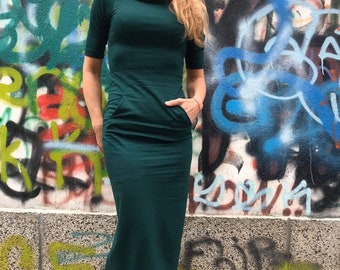 May include: A long, dark green maxi dress with a cowl neck and two pockets. The dress is made of a soft, stretchy fabric.