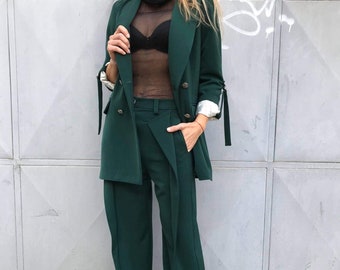 May include: A dark green blazer with long sleeves and a matching pair of wide-leg pants. The blazer has a double-breasted closure and gold buttons. The pants have a high waist and a pleated front.
