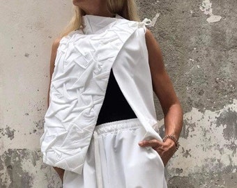 May include: A white sleeveless top with a unique, geometric design and a white pair of pants with a drawstring waist. The pants have a loose, flowing fit.
