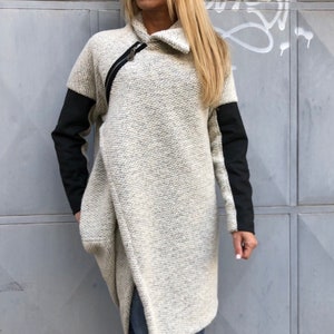 May include: A long, asymmetrical, off-white sweater with black sleeves. The sweater has a zipper detail on the front and a high collar.