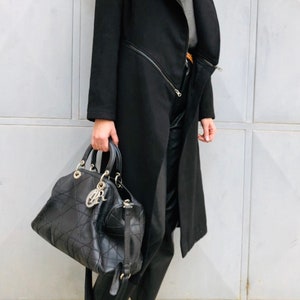 May include: A black long coat with a zipper detail and a black leather handbag. The person is wearing brown suede loafers.
