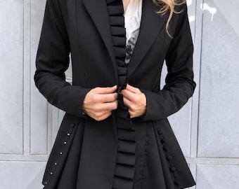 May include: A black blazer featuring a vertical pleated ruffle trim along the front opening, a notched lapel, and a flared peplum hem. The garment is detailed with rows of small, round black buttons along the side panels of the waist.