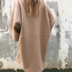 Może przedstawiać: Długi, oversize'owy, brązowy płaszcz wełniany o luźnym kroju. Płaszcz ma wysoki kołnierz i długie rękawy.