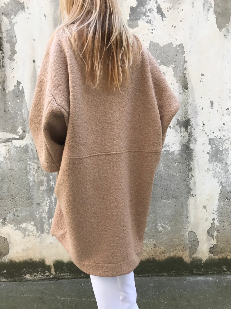 Może przedstawiać: Długi, oversize'owy, brązowy płaszcz wełniany o luźnym kroju. Płaszcz ma wysoki kołnierz i długie rękawy.