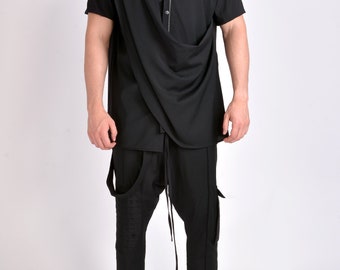 Puede incluir: Conjunto negro de dos piezas. La parte superior es una camisa de manga corta con un diseño asimétrico drapeado y un detalle de cremallera. Los pantalones son negros con bolsillos y tirantes. El conjunto se combina con zapatillas blancas.