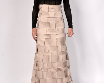 May include: A long, beige skirt made of woven fabric panels. The skirt has a fitted waist and a flowing, A-line silhouette.
