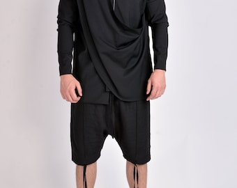 Puede incluir: Camisa negra de manga larga con un diseño asimétrico drapeado y cuello mandarín. El conjunto incluye pantalones cortos negros a juego con detalles de cordón y zapatillas altas. El conjunto es de estilo moderno y vanguardista.