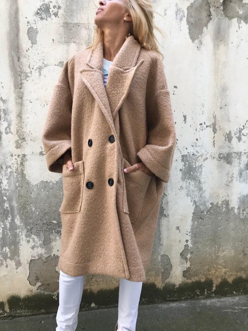 Może przedstawiać: Długi, dwurzędowy płaszcz w kolorze camel z dużymi kieszeniami. Płaszcz wykonany jest z miękkiej, puszystej tkaniny.